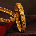 Gold bangles in 18k gold with intricate textured patterns and embedded red gemstones for fine jewelry trends