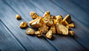 Irregular gold nuggets with a shiny metallic sheen on dark blue wood illustrating gold purity for engagement rings at everett jewelry store.