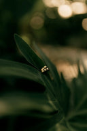 Two interlocking 18k gold engagement rings rest elegantly on a dark green leaf showcasing art gold jewelry craftsmanship