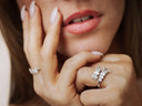 Woman's hand wearing diamond rings near her face
