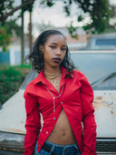 A woman wearing a vibrant red button-up shirt and blue jeans in an article about 18k gold jewelry and royal jewels symbolism