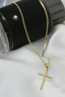 A gold cross necklace sitting on top of a black cup