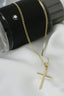 A gold cross necklace sitting on top of a black cup