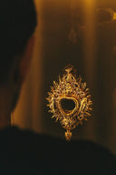 Golden ornate heart-shaped religious pendant with intricate filigree and sunburst design from art gold jewelry collection