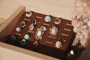 A collection of ornate gold jewelry rings with various gemstones displayed on a dark brown wooden tray for fine jewelry