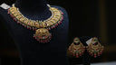 Gold jewelry necklace with intricate filigree design and red green gemstones displayed on black bust for art gold jewelry article.