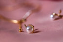 A delicate gold jewelry stud earring with a single white pearl in an elegant curved art gold setting.