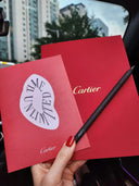 A sleek black Cartier pencil with textured grip and gold branding on vibrant red packaging highlighting fine jewelry.