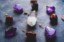 A clear faceted quartz crystal with internal inclusions displayed with purple and deep red gemstones for fine jewelry.