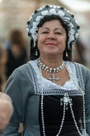 Gray and white lace-trimmed historical costume with pearl necklace and cross pendant in fine jewelry context