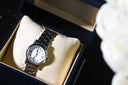 A sleek silver-toned wristwatch with white dial and roman numerals complements art gold jewelry in elegance.