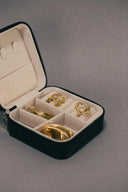 Black zippered jewelry case with cream compartments holding gold-toned engagement rings in fine jewelry collection