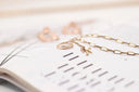 Gold jewelry featuring an 18k gold chain necklace with a small initial charm and two stacked fine jewelry rings displayed nearby