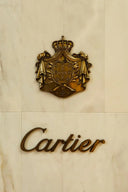 Gold-toned cartier crest plaque with intricate heraldic design and crown mounted on marble wall in art gold jewelry context