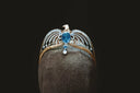 A golden eagle-themed tiara featuring a central blue gemstone and clear crystals in fine art gold jewelry design.
