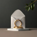 A gold engagement ring with a diamond centerpiece and matching band in a white envelope from Art Gold jewelry.