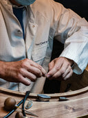 A jeweler in a van cleef arpels lab coat handling fine jewelry components on a wooden workbench focusing on gold jewelry