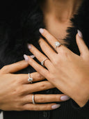 A woman’s hand wearing four unique diamond rings in silver-toned settings featured in a 18k gold jewelry care guide