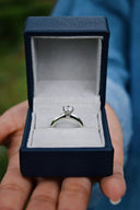 A sparkling diamond solitaire engagement ring in a silver band displayed in a navy box for art gold jewelry enthusiasts.