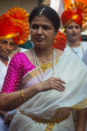 A woman in white saree with gold border and art gold jewelry including pearl necklaces and golden bangles.