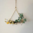 A triangular brass frame wreath with dried eucalyptus and yellow berries illustrating art gold in fine jewelry craft