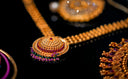 Gold necklace with an ornate round pendant featuring red and purple gemstones in fine 18k gold jewelry style