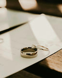 A pair of silver wedding bands with a central diamond engagement ring and a smooth band in modern heirloom style.