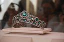 An ornate silver tiara with emerald stones and diamonds exemplifies crown jewels and fine jewelry traditions.