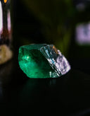 A rough, uncut emerald gemstone with vibrant green hues.