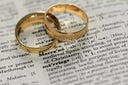 Two interlocking gold wedding bands made of fine art gold jewelry rest on an open dictionary page.