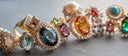 A collection of custom gold jewelry wedding bands and engagement rings with vibrant central gemstones and diamond accents