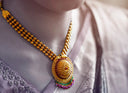 Gold necklace with intricate beadwork and an oval pendant featuring red green and purple gemstones in 18k gold jewelry