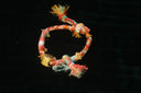 A colorful hand-knotted rope bracelet with frayed ends and a gold bell charm featured in art gold jewelry Everett listings.