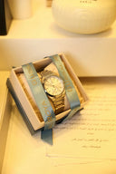 Gold-tone stainless steel bracelet watch with cream dial and blue satin ribbon in article on engagement rings and wedding bands