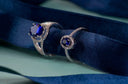 A pair of elegant silver royal engagement rings with deep blue sapphire stones surrounded by sparkling diamonds.