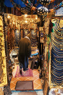 A man in a dark coat stands inside a vibrant shop filled with gold jewelry and fine jewelry including gold rings.