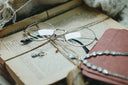 Round-framed reading glasses with thin metallic rims and black temple tips resting on an open book in fine jewelry context