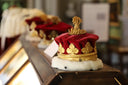 A regal red velvet crown with intricate art gold leaf embellishments and white fur trim showcasing fine jewelry.
