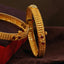 A pair of gold bracelets sitting on top of a velvet cushion