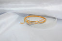 Gold-toned bangle with sleek intertwined design and sparkling clear stones exemplifies fine gold jewelry trends.