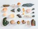 A collection of polished and raw cursed gems including heart-shaped agate and tiger eye spheres for 18k gold jewelry.