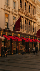 The luxurious Cartier storefront with elegant red awnings showcases fine jewelry in 18k gold against a classical facade.