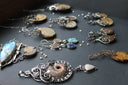 A silver filigree pendant with a detailed ammonite fossil centerpiece and teardrop charm for fine jewelry collections.