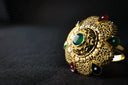 Ornate gold engagement ring with central emerald and green red gemstones featured at everett jewelry store