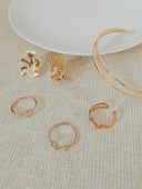A set of rose gold-toned art gold jewelry featuring delicate flower earrings, geometric open band gold rings, and a double-layered bangle.