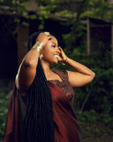 A woman with braided hair and gold jewelry smiles.