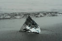 Translucent jagged ice gem with crystalline blue tint on dark sand shore