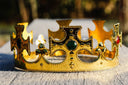 Gold jewelry crown with intricate cross and fleur-de-lis designs featuring a central green gemstone and fine jewelry stones