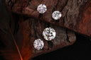 Four brilliant cut clear diamonds on textured dark brown wood illustrating fine jewelry and art gold traditions.