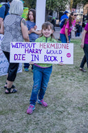Young girl with protest sign amid Harry Winston art gold jewelry opulence
